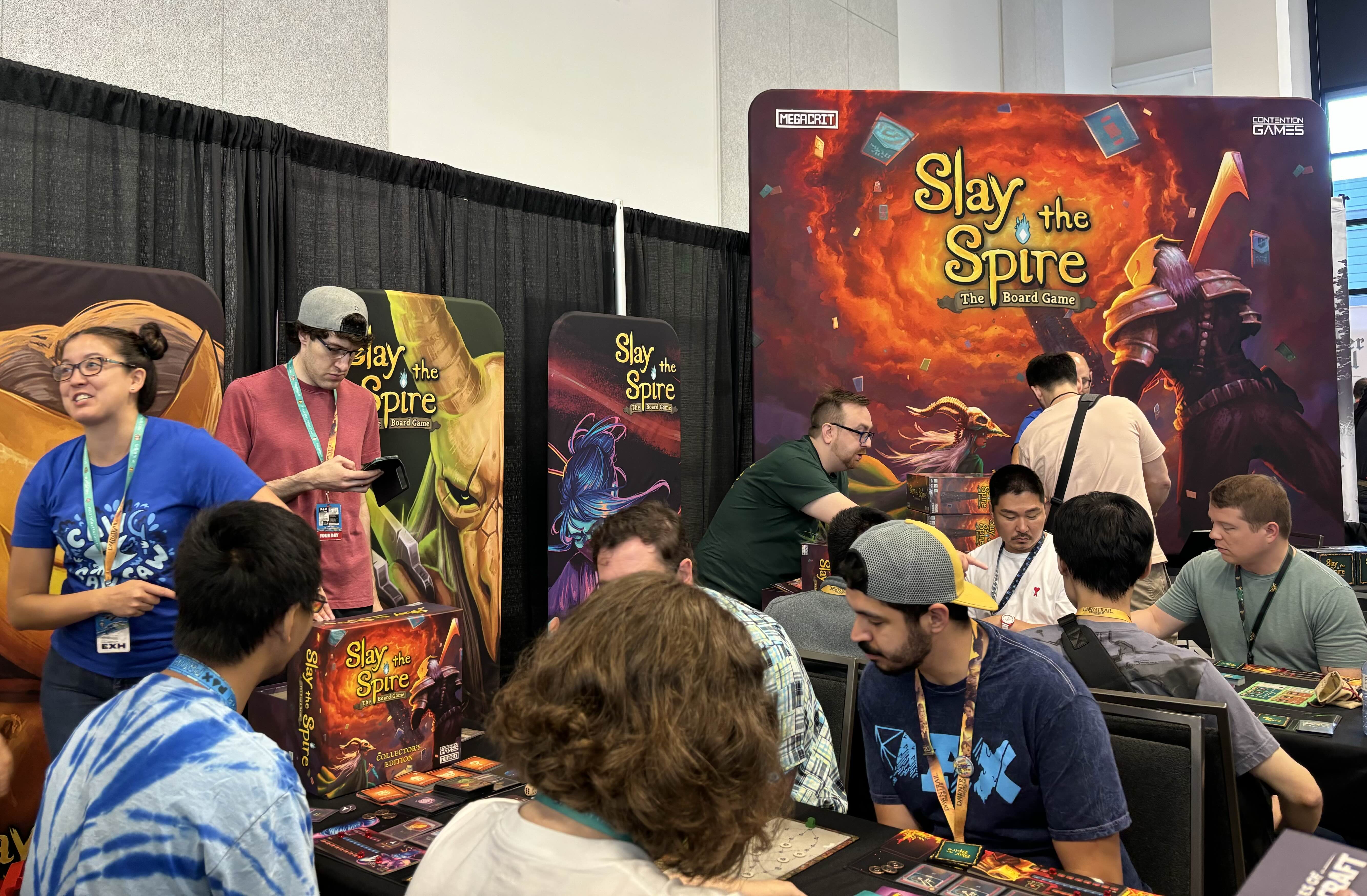 An image of Contention Games’ booth at PAX West, with big Slay the Spire banners and lots of players sitting at tables demoing the board game.