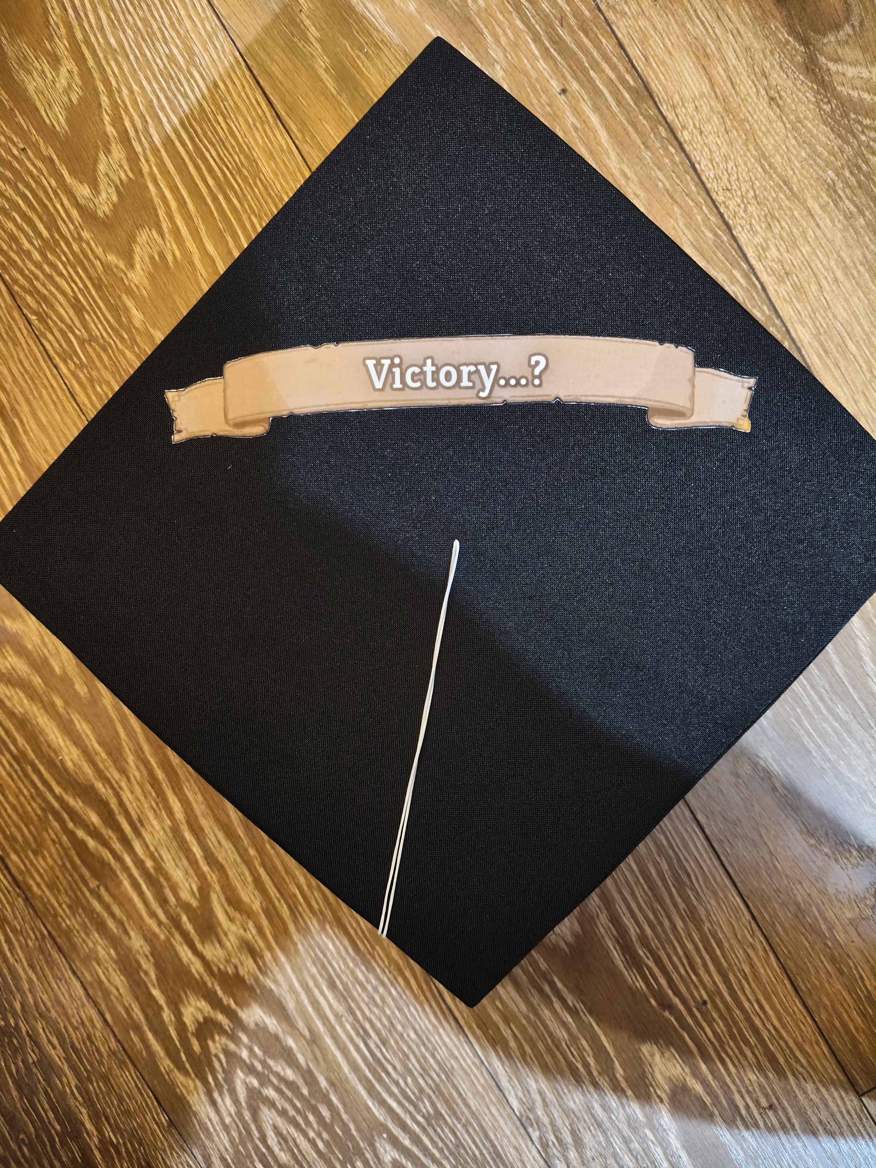 A graduation cap that has the game over “Victory…?” quote tacked onto it.